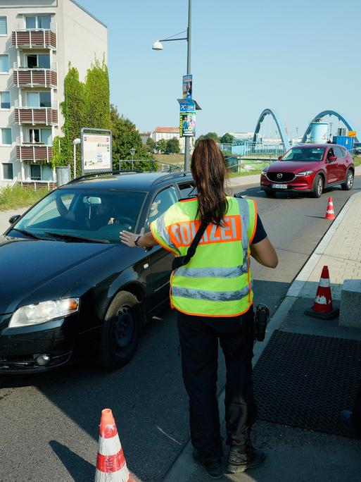 Eine Polizistin und ein Polizist nehmen Grenzkontrollen vor und stoppen dafür Autos.