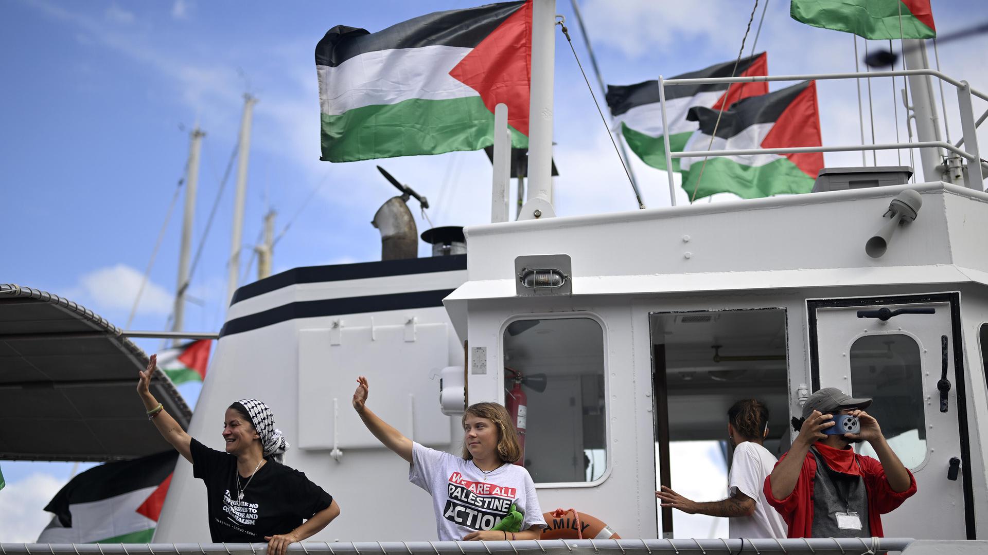 Greta Thunberg steht auf einem Schiff und winkt. Darüber weht die palästinensische Flagge. Greta Thunberg steht auf einem Schiff und winkt. Darüber weht die palästinensische Flagge.