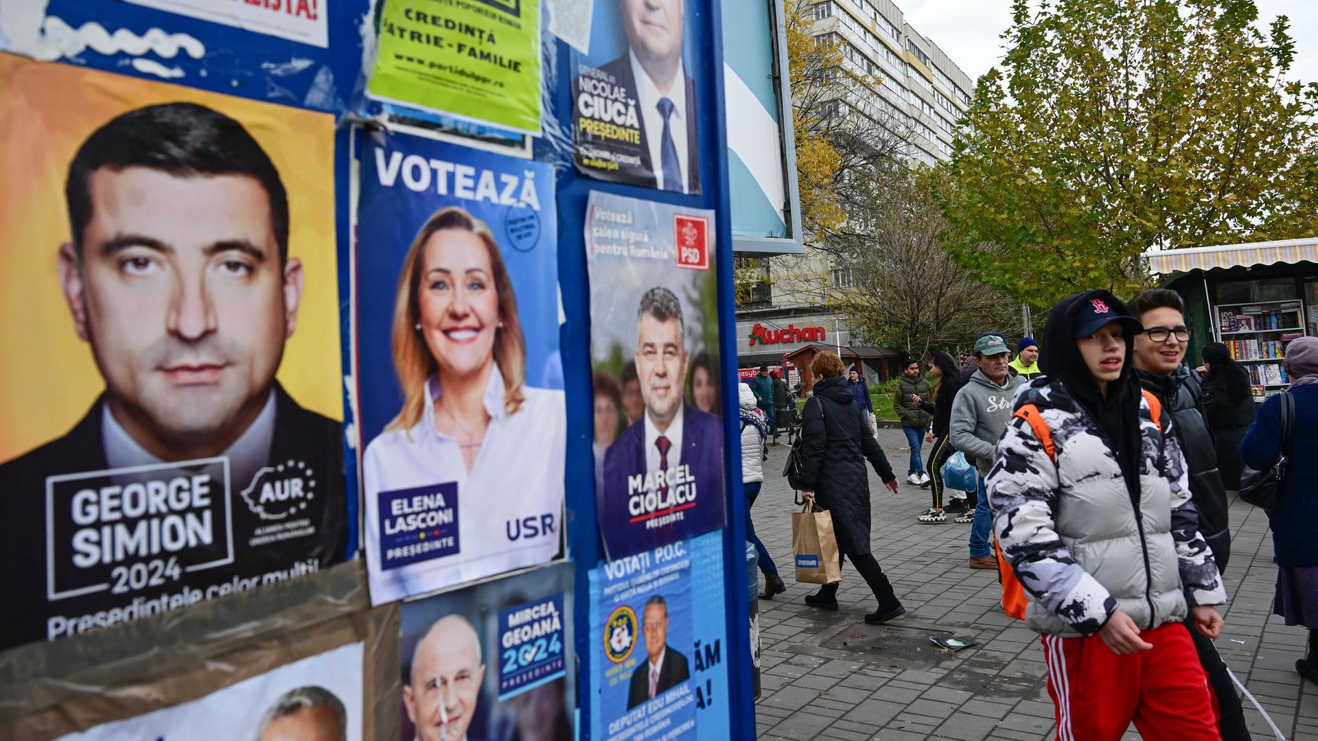 Wahlplakate in der rumänischen Hauptstadt Bukarest. Im Hintergrund ist ein Hochhaus zu erkennen. An den Plakaten gehen Menschen in Winterkleidung vorbei. 