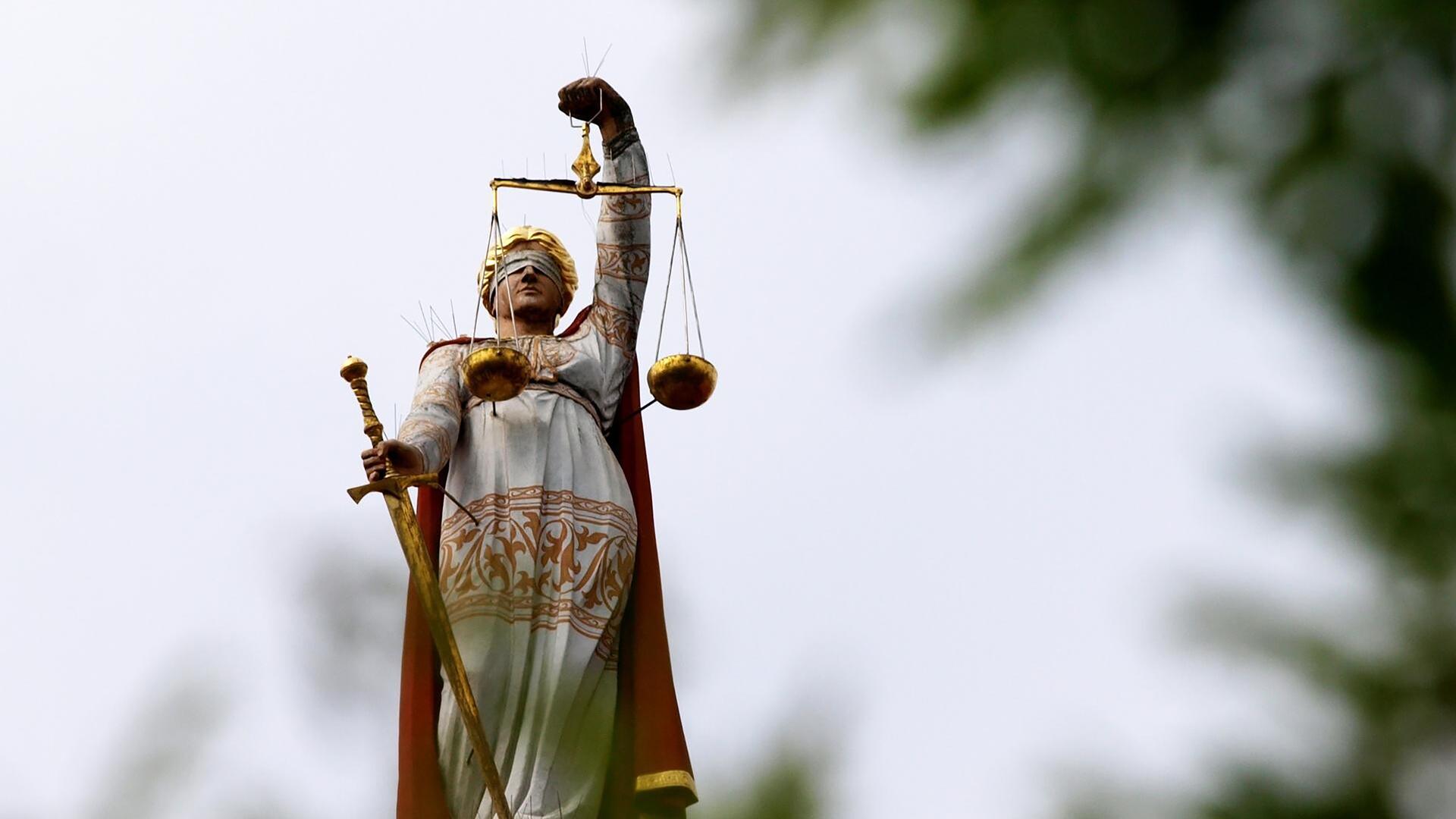 Froschperspektive auf eine Justitia-Figur. Im Vordergrund in der Unschärfe ein Baum. (Symbolbild) Froschperspektive auf eine Justitia-Figur. Im Vordergrund in der Unschärfe ein Baum. (Symbolbild)