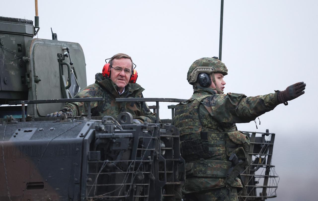 Bundesverteidigungsminister Pistorius sitzt mit Ohrschützern auf einem Panzer. Ein Soldat erklärt ihm etwas.