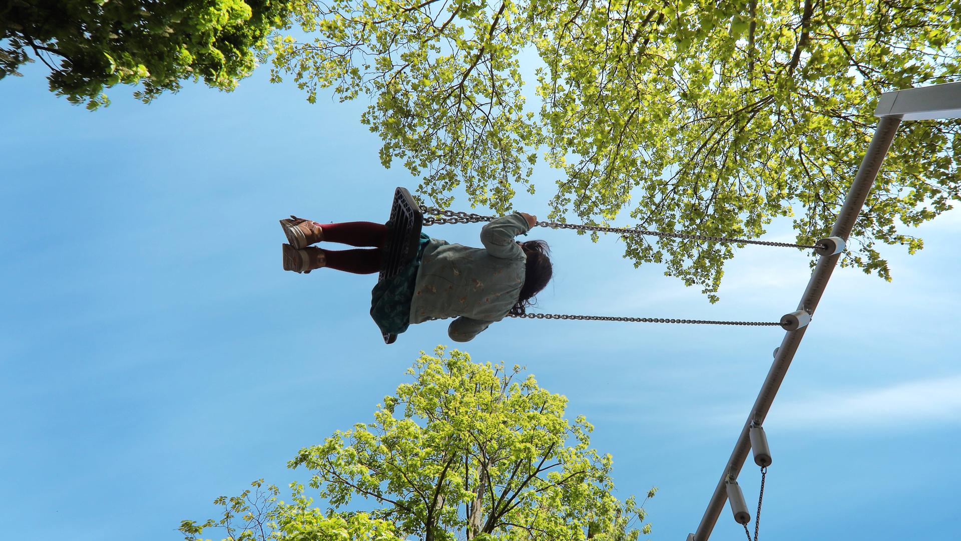 Auf einem Spielplatz, ein Mädchen schaukelt glücklich zwischen den Bäumen.