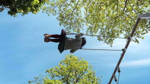 Auf einem Spielplatz, ein Mädchen schaukelt glücklich zwischen den Bäumen. Auf einem Spielplatz, ein Mädchen schaukelt glücklich zwischen den Bäumen.