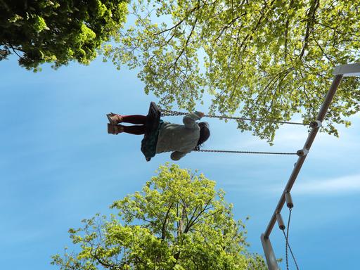 Auf einem Spielplatz, ein Mädchen schaukelt glücklich zwischen den Bäumen.