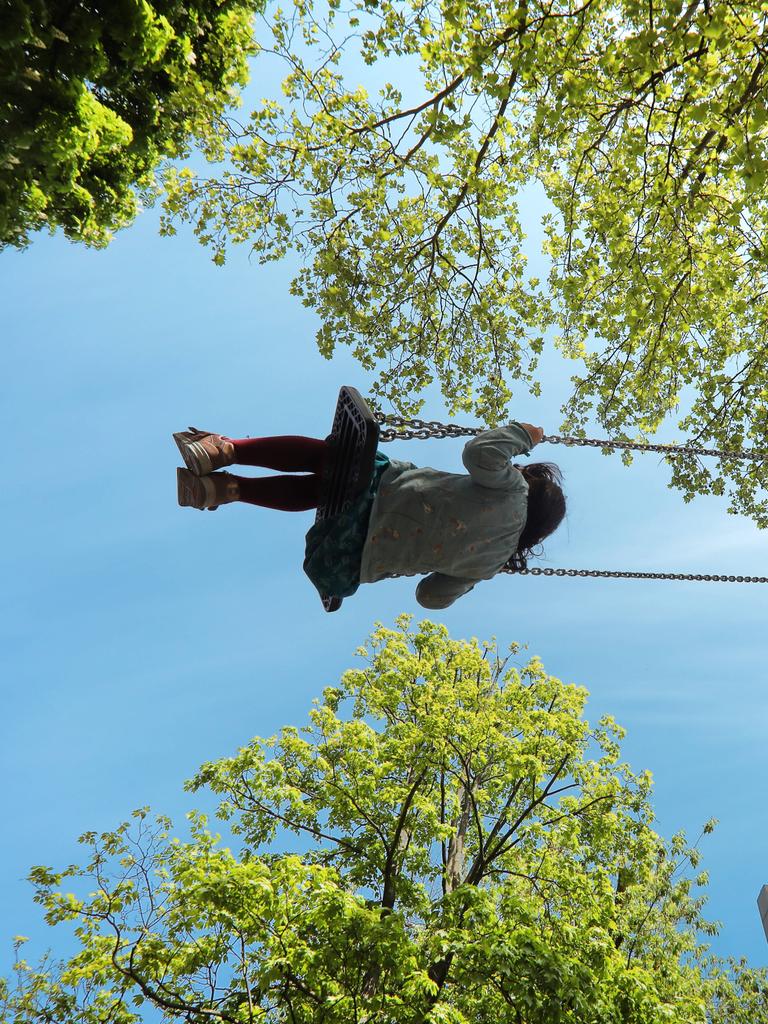 Auf einem Spielplatz, ein Mädchen schaukelt glücklich zwischen den Bäumen.