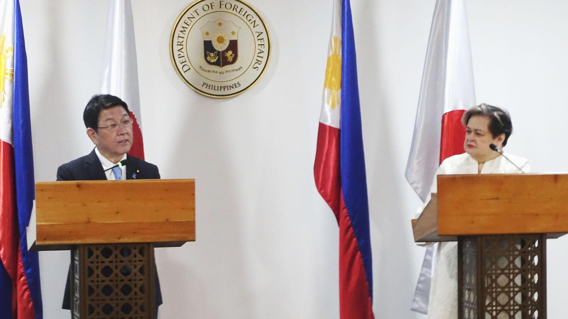 Der japanische Außenminister und seine philippinische Kollegin Motegi stehen nebeneinander an jeweiligen Rednerpulten. Der japanische Außenminister und seine philippinische Kollegin Motegi stehen nebeneinander an jeweiligen Rednerpulten.