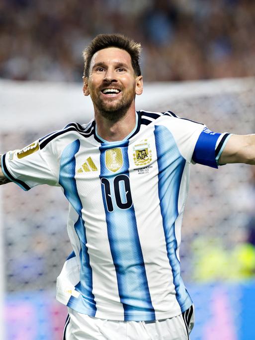 Lionel Messi läuft im blau-weiß gestreiften Trikot mit ausgebreiteten Armen über den Fußballrasen, im Hintergrund sind verschwommen ein Tor und Zuschauer zu sehen. Lionel Messi läuft im blau-weiß gestreiften Trikot mit ausgebreiteten Armen über den Fußballrasen, im Hintergrund sind verschwommen ein Tor und Zuschauer zu sehen.