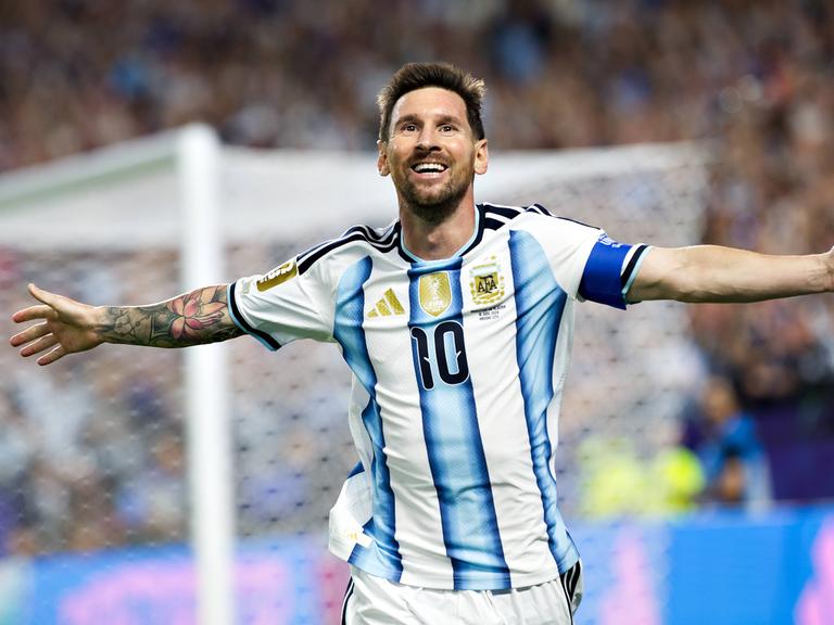 Lionel Messi läuft im blau-weiß gestreiften Trikot mit ausgebreiteten Armen über den Fußballrasen, im Hintergrund sind verschwommen ein Tor und Zuschauer zu sehen. Lionel Messi läuft im blau-weiß gestreiften Trikot mit ausgebreiteten Armen über den Fußballrasen, im Hintergrund sind verschwommen ein Tor und Zuschauer zu sehen.