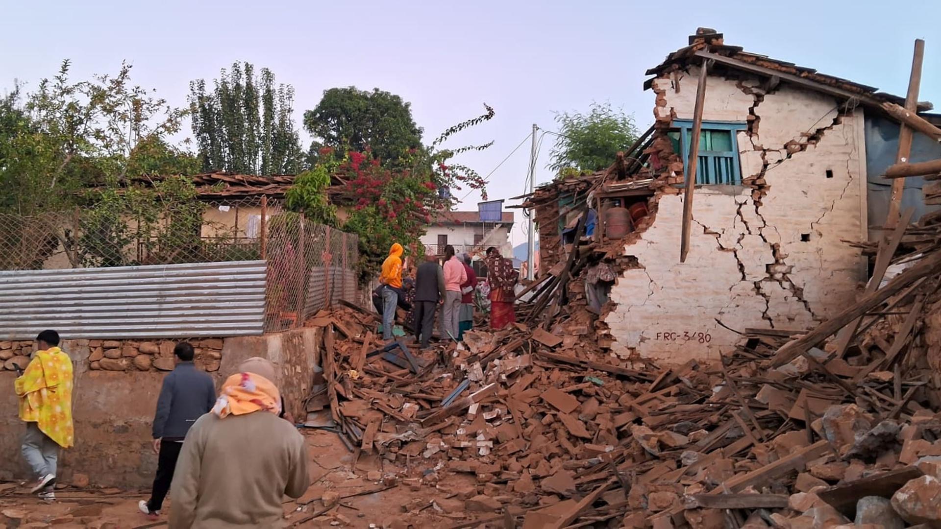Menschen steigen über Schutt und suchen in den Trümmern nach ihren Habseligkeiten. Ein Haus ist zur Hälfte eingestürzt.