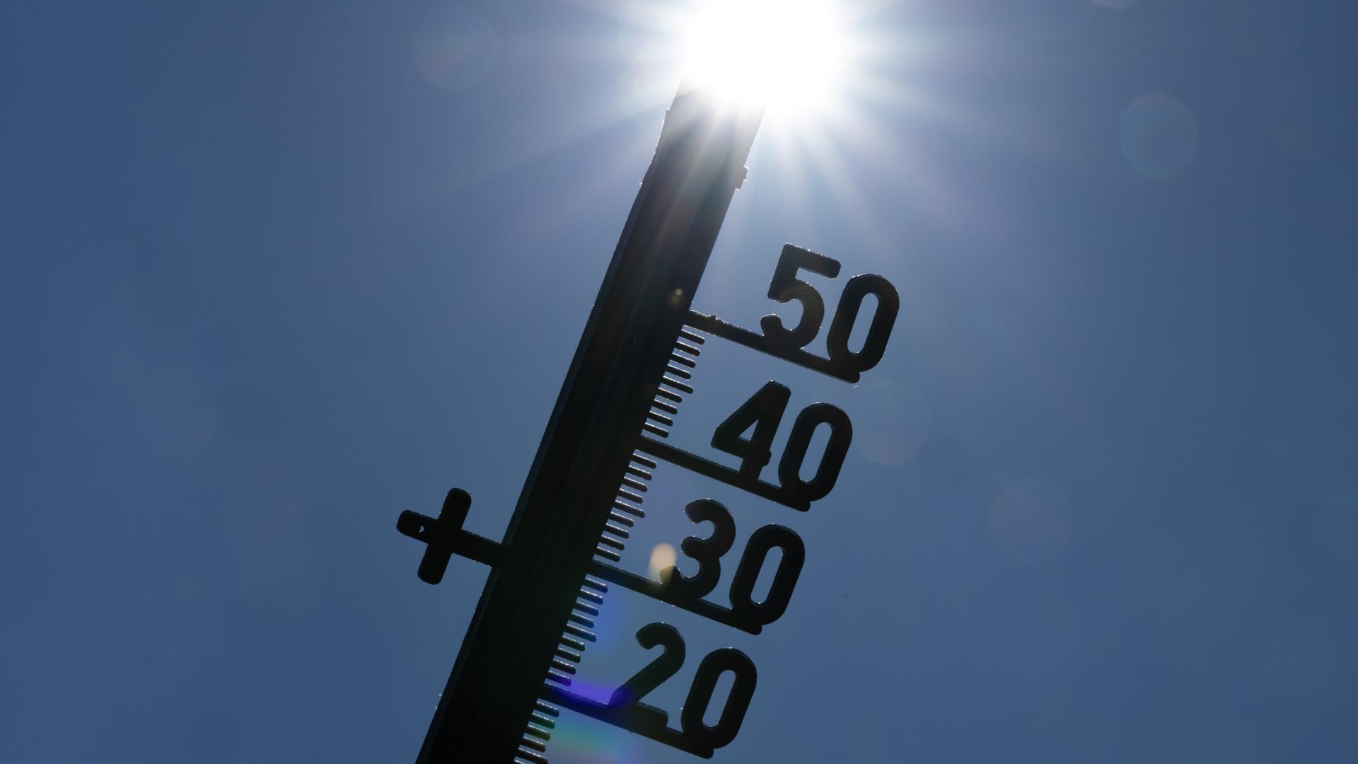 Vor dem Licht der gleißenden Mittagssonne zeichnet sich die Silhouette eines Thermometers ab.