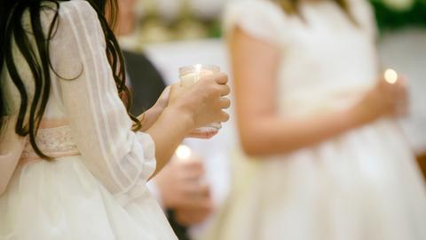 Junge Mädchen, deren Gesichter nicht zu erkennen sind, halten eine Kerze im Glas in der Hand. Sie tragen festliche weiße Kleidung.