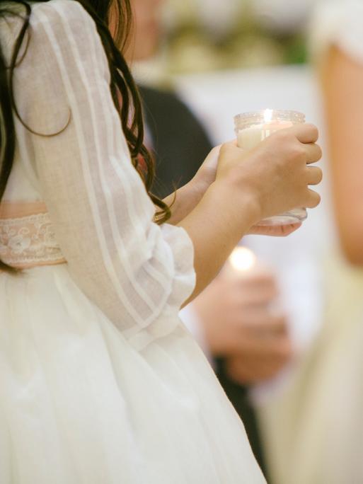 Junge Mädchen, deren Gesichter nicht zu erkennen sind, halten eine Kerze im Glas in der Hand. Sie tragen festliche weiße Kleidung.