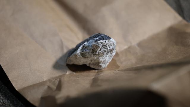 Ein Teil von einem Meteorit liegt auf einer Papier-Tüte.