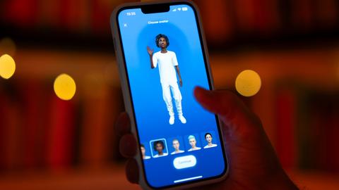 Eine Hand hält ein Smartphone auf dem eine virtuelle Person zu sehen ist, die in die Kamera blickt. 