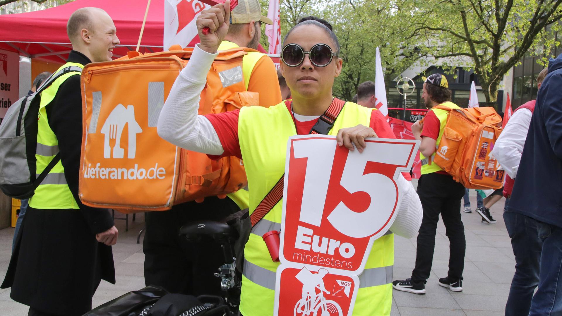 Bei einer Streikaktion der Lieferandofahrer in Dortmund hält eine Frau ein Plakat mit der Aufschrift "15 Euro".