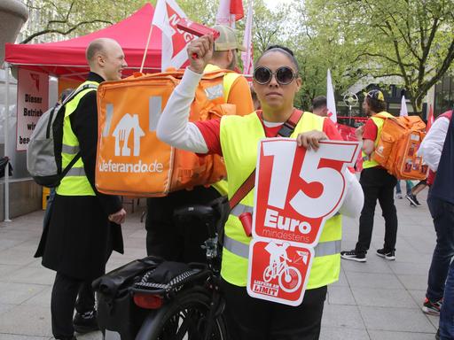 Bei einer Streikaktion der Lieferandofahrer in Dortmund hält eine Frau ein Plakat mit der Aufschrift "15 Euro".