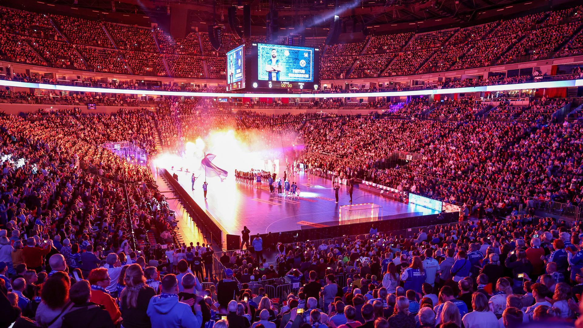 Blick in die abgedunkelte KölnArena, eine sehr große Sporthalle, die Ränge voller Zuschauer, in der Mitte das Handballfeld, auf dem mit Lichteffekten die Mannschaften einlaufen.