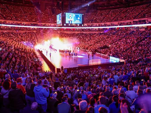 Blick in die abgedunkelte KölnArena, eine sehr große Sporthalle, die Ränge voller Zuschauer, in der Mitte das Handballfeld, auf dem mit Lichteffekten die Mannschaften einlaufen.