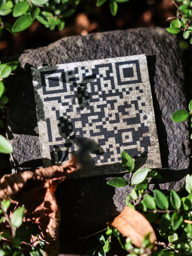 Ein QR-Code liegt zwischen Planzen auf einer Grabstätte auf dem Melaten-Friedhof in Köln. Ein QR-Code liegt zwischen Planzen auf einer Grabstätte auf dem Melaten-Friedhof in Köln.
