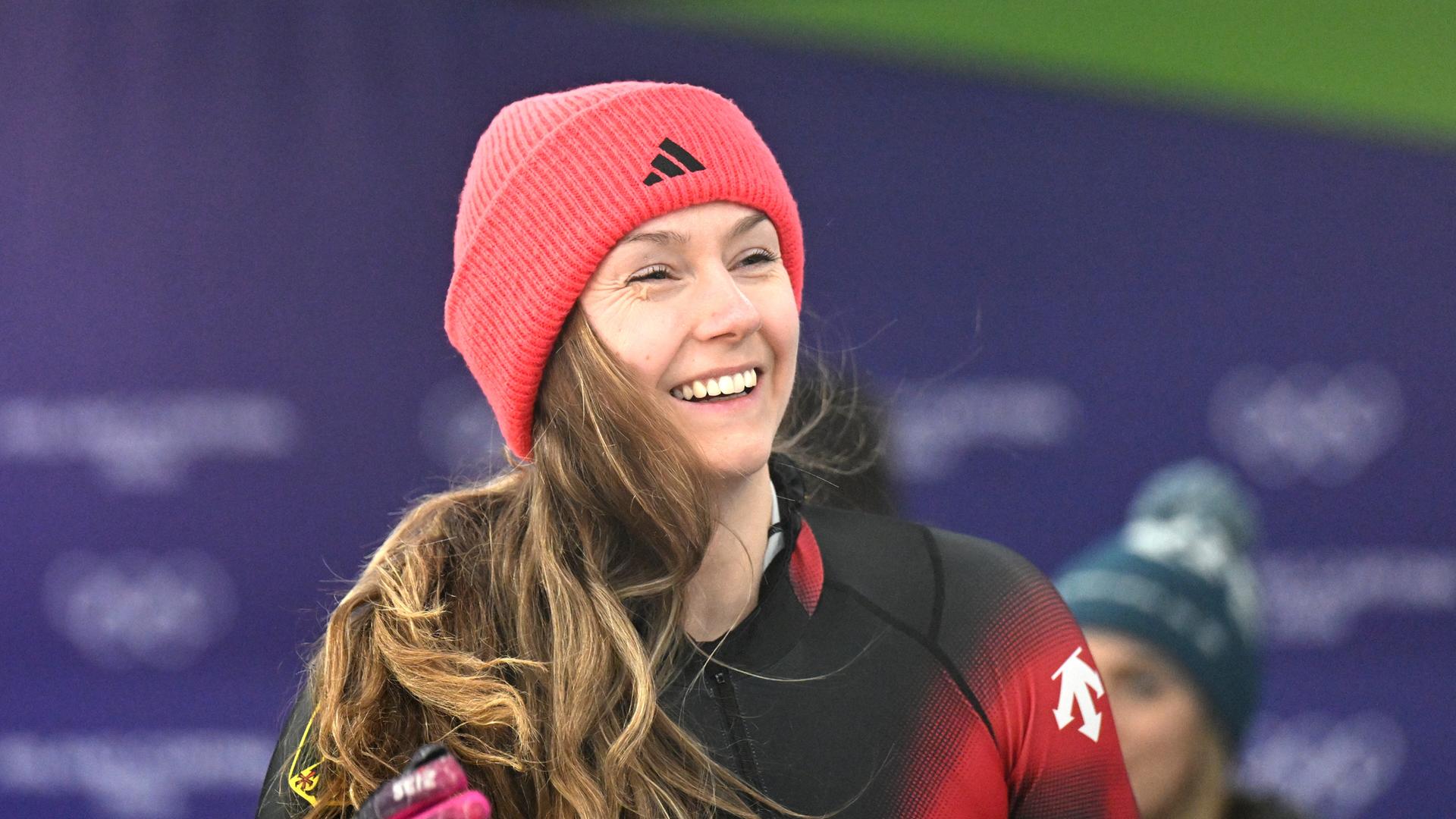 Das Bild zeigt Laura Nolte bei den Olympischen Winterspielen 2026 startbereit in Sportkleidung für den Zweierbob. Sie lächelt in die Kameras. Das Bild zeigt Laura Nolte bei den Olympischen Winterspielen 2026 startbereit in Sportkleidung für den Zweierbob. Sie lächelt in die Kameras.