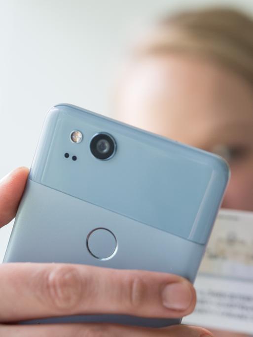 Eine Frau hält am 23.01.2018 in Berlin ein Smartphone und einen Personalausweis in den Haenden, um am Video-Ident-Verfahren teilzunehmen (gestellte Szene). Foto: Andrea Warnecke