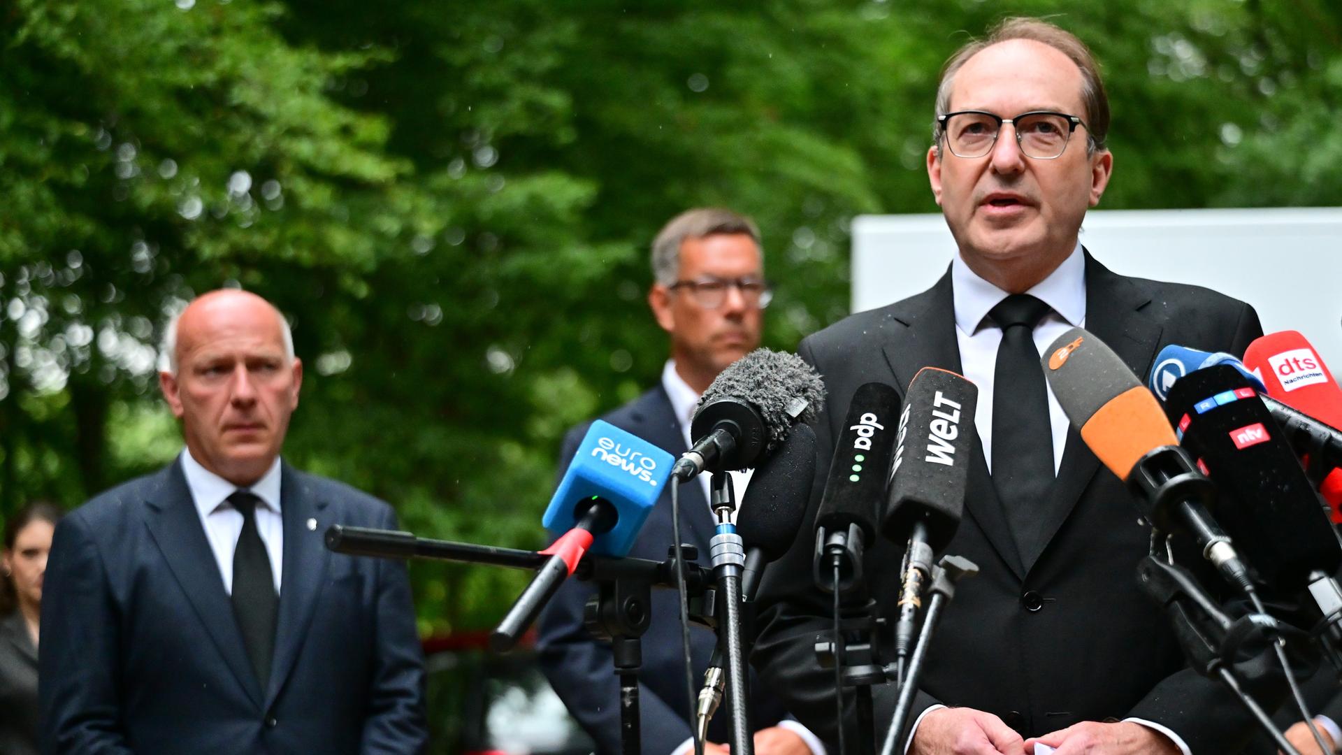 Alexander Dobrindt steht an zahlreichen Mikrofonen und gibt ein Statement ab. Im Hintergrund sind Kai Wegner und eine Grünanlage zu erkennen. 