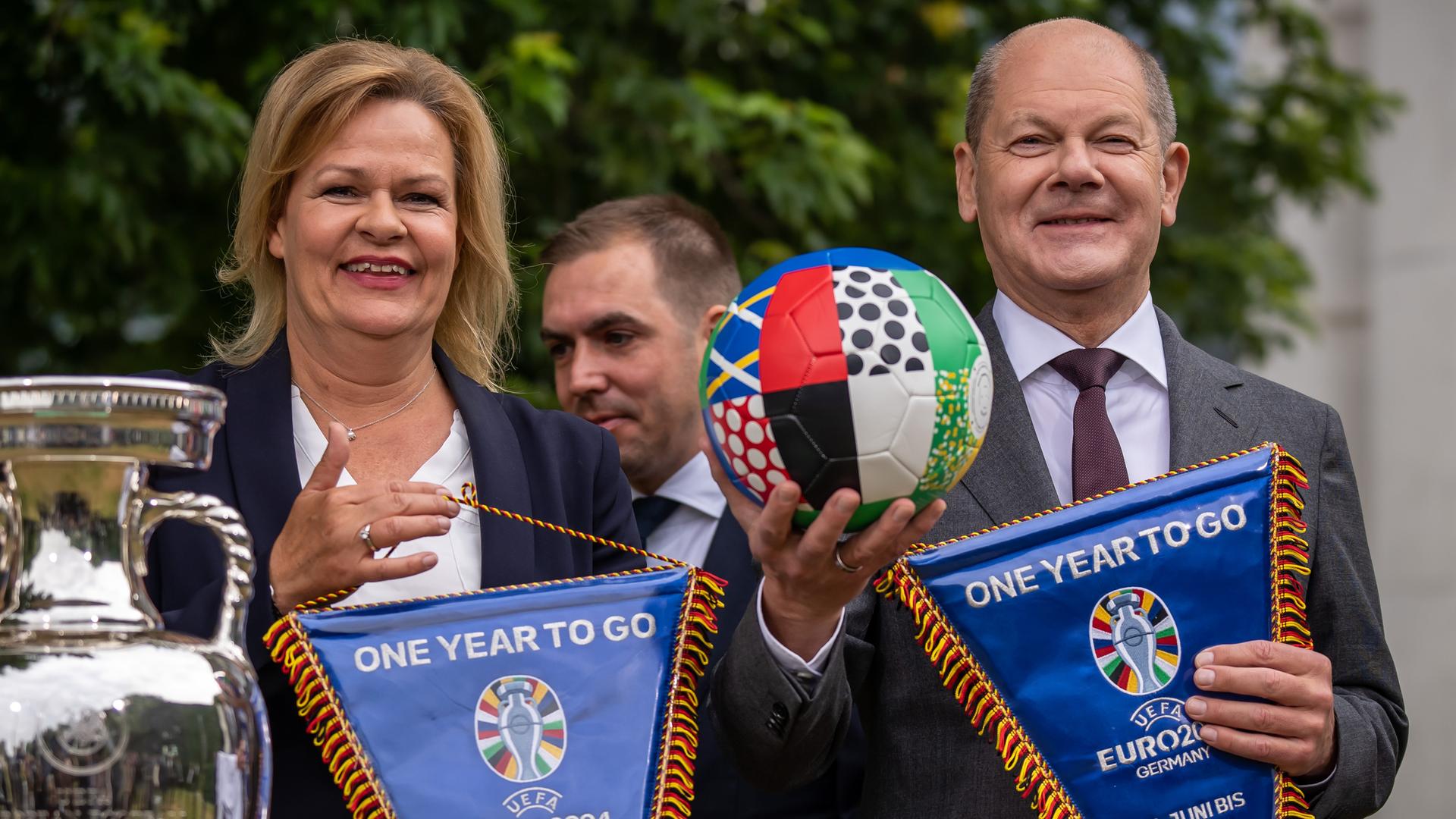 Bundeskanzler Olaf Scholz hält in der rechten Hand einen Fußball, neben ihm steht Bundesinnenministerin Faeser, in der Mitte ist der Turnierdirektor und ehemalige Fußballnationalspieler Philipp Lahm zu sehen. Bundeskanzler Olaf Scholz hält in der rechten Hand einen Fußball, neben ihm steht Bundesinnenministerin Faeser, in der Mitte ist der Turnierdirektor und ehemalige Fußballnationalspieler Philipp Lahm zu sehen.