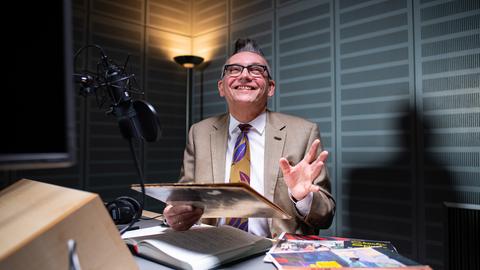 Moderator Götz Alsmann sitzt im WDR-Tonstudio in Münster vor dem Mikrofon und hält ein altes Plattencover in der Hand.
