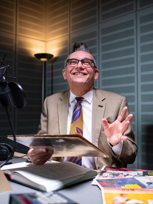 Moderator Götz Alsmann sitzt im WDR-Tonstudio in Münster vor dem Mikrofon und hält ein altes Plattencover in der Hand.