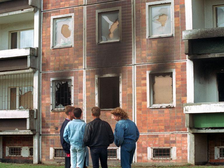 Jugendliche stehen vor einem Hochhaus in Lichtenhagen mit ausgebranntem Erdgeschoss.