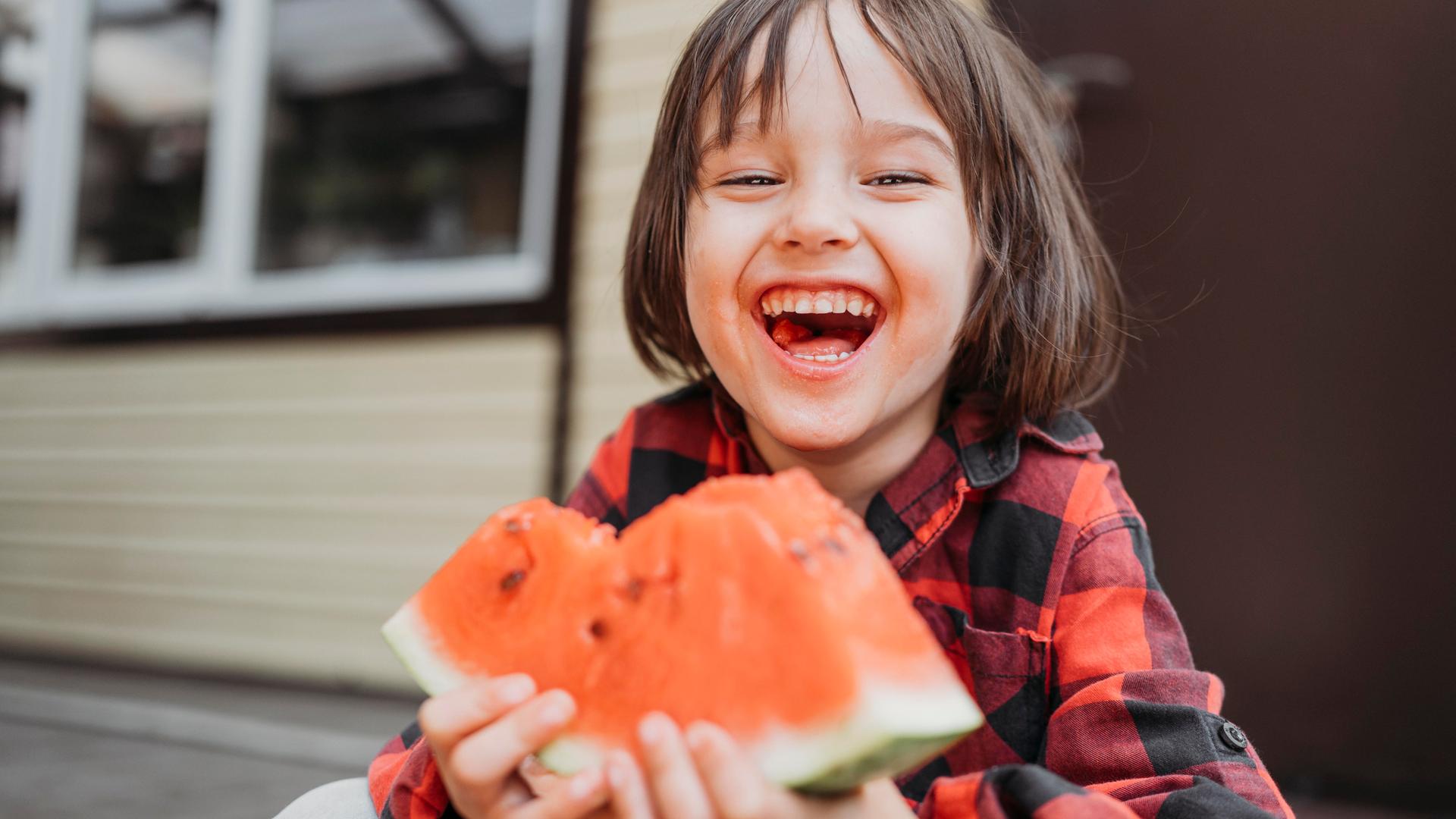Ein lachender Junge mit einem Stück Melone in der Hand. 