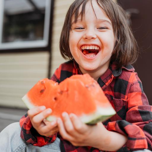 Ein lachender Junge mit einem Stück Melone in der Hand. 