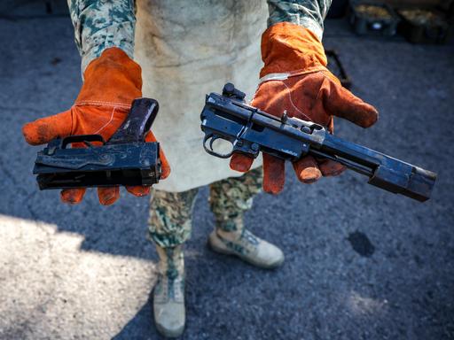 Eine Person in Militäruniform hält zwei Waffen mit abgesägten Läufen in die Kamera.