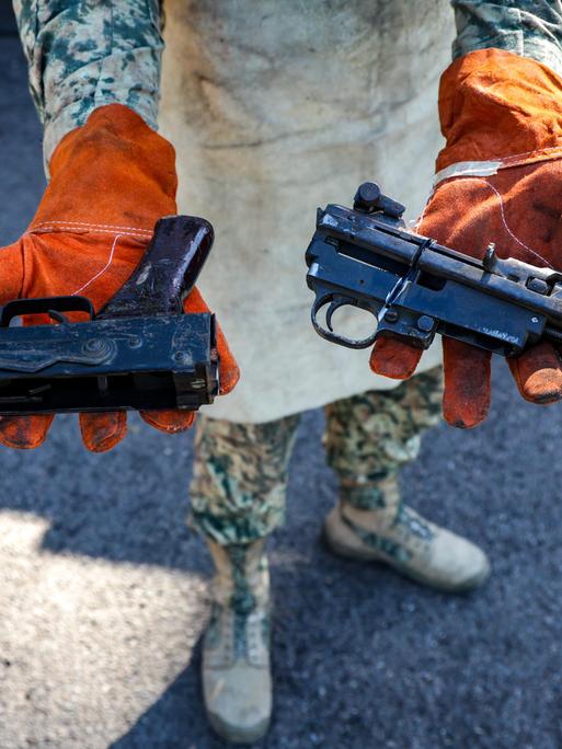 Eine Person in Militäruniform hält zwei Waffen mit abgesägten Läufen in die Kamera.