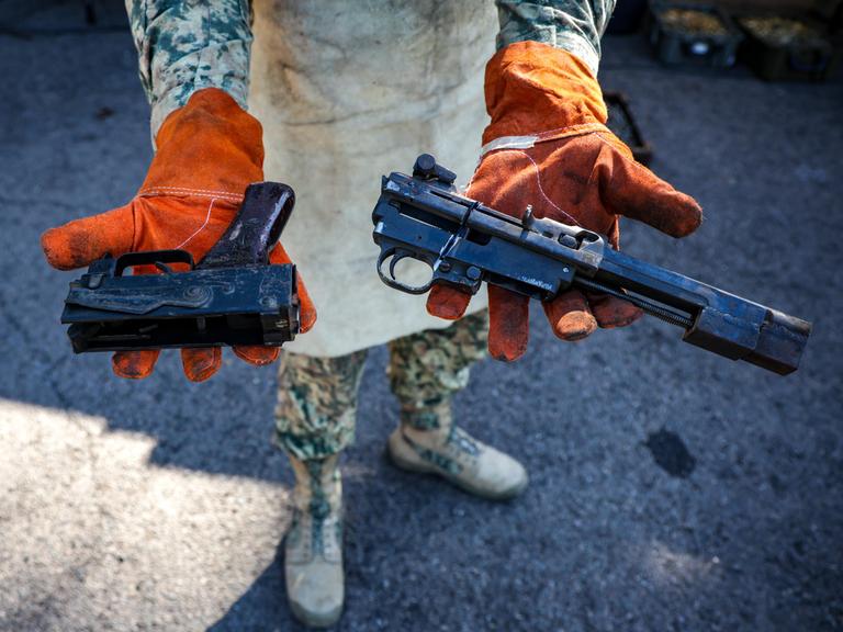 Eine Person in Militäruniform hält zwei Waffen mit abgesägten Läufen in die Kamera.