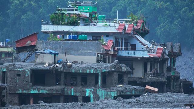 Auf dem Bild sieht man ein Haus in Nepal. Das Haus steht an einem Fluss. Nach einer großen Überschwemmung ist dort noch viel Schlamm.