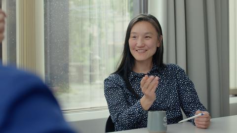 Saikal Zhunush sitzt an einem Tisch und spricht gestikulierend.