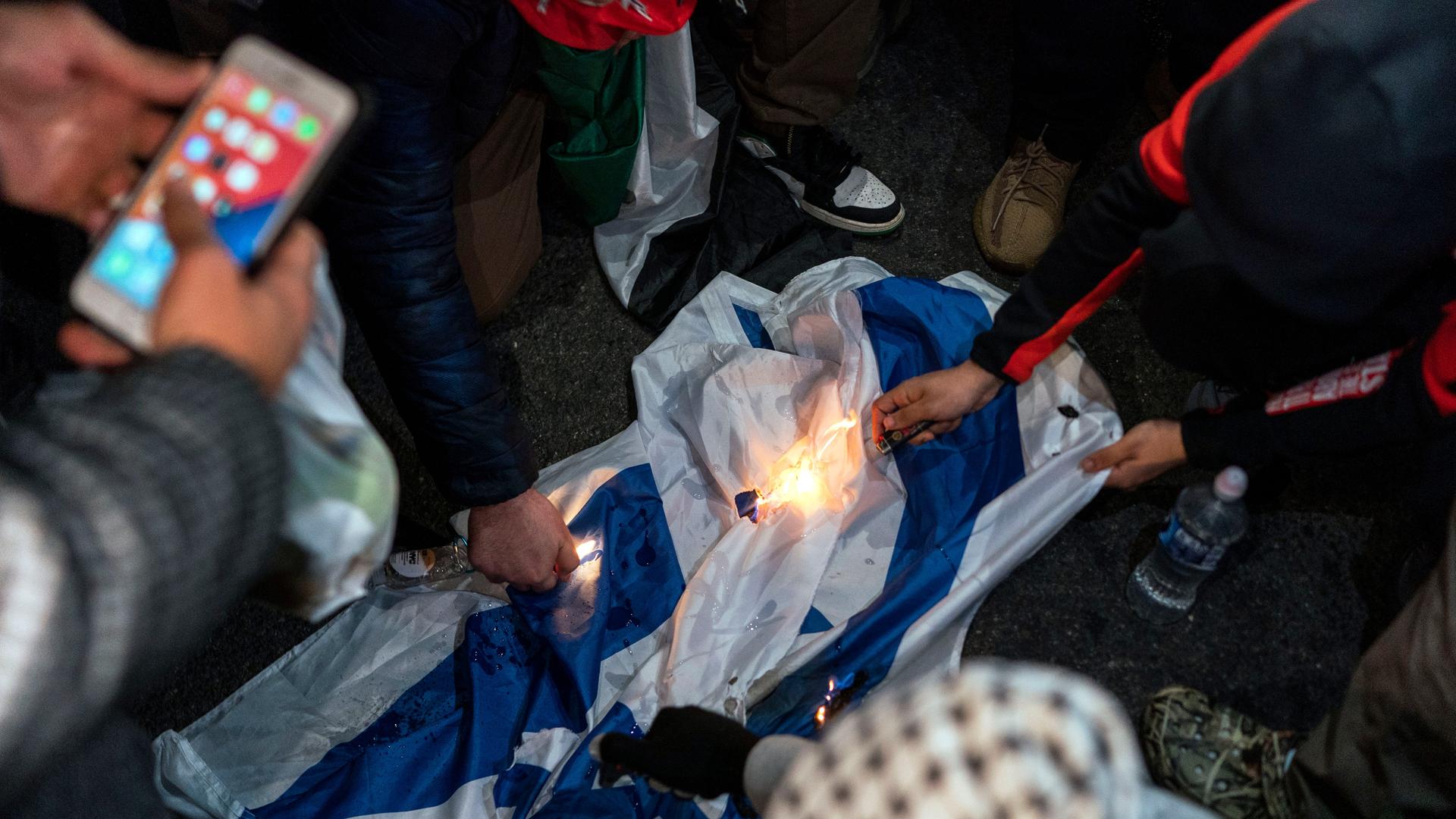 Detailaufnahme von Demonstranten, die während eines Protests eine Israelflagge anzünden.