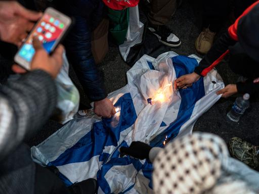 Detailaufnahme von Demonstranten, die während eines Protests eine Israelflagge anzünden.