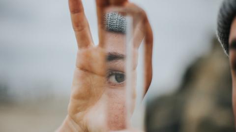 Eine Frau betrachtet sich in einem Stück einer Spiegelfläche in ihren Händen.