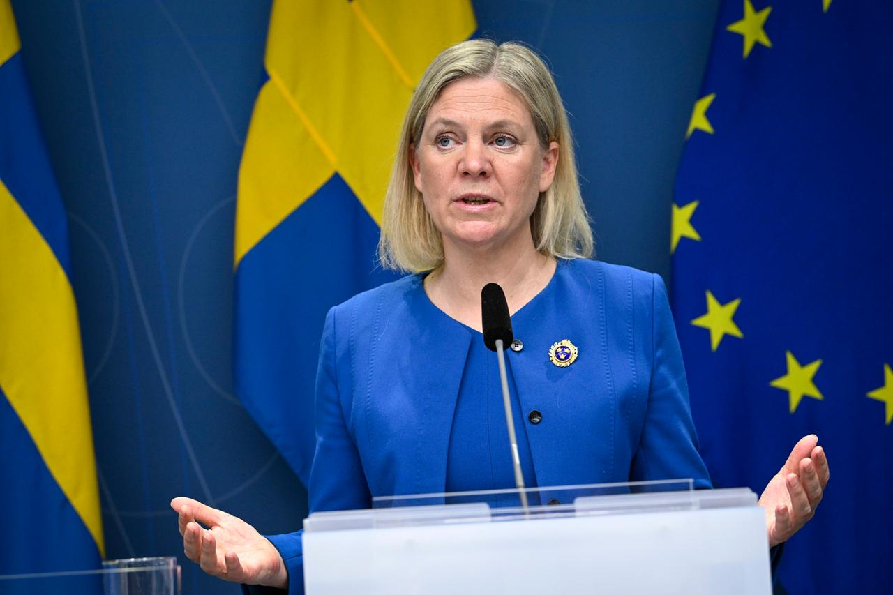 Das Bild zeigt die schwedische Ministerpräsidentin Magdalena Andersson an einem Rednerpult bei einer Konferenz in Stokholm vor der EU-Flagge und der schwedischen Flagge. Sie trägt einen blauen Anzug.