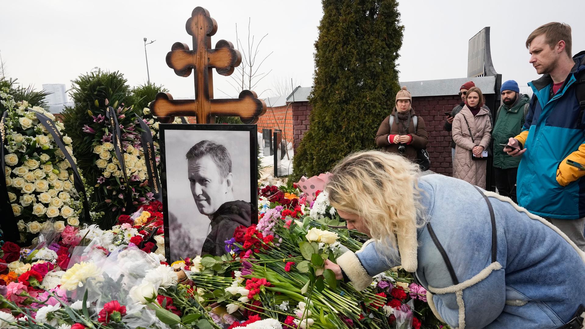 Eine Frau legt einen Tag nach der Beerdigung von Alexej Nawalny auf dem Borisowskoje-Friedhof Blumen am Grab ab. Auf dem Grab stehen ein schwarz-weißes Porträt von Nawalny und ein orthodoxes Kreuz.