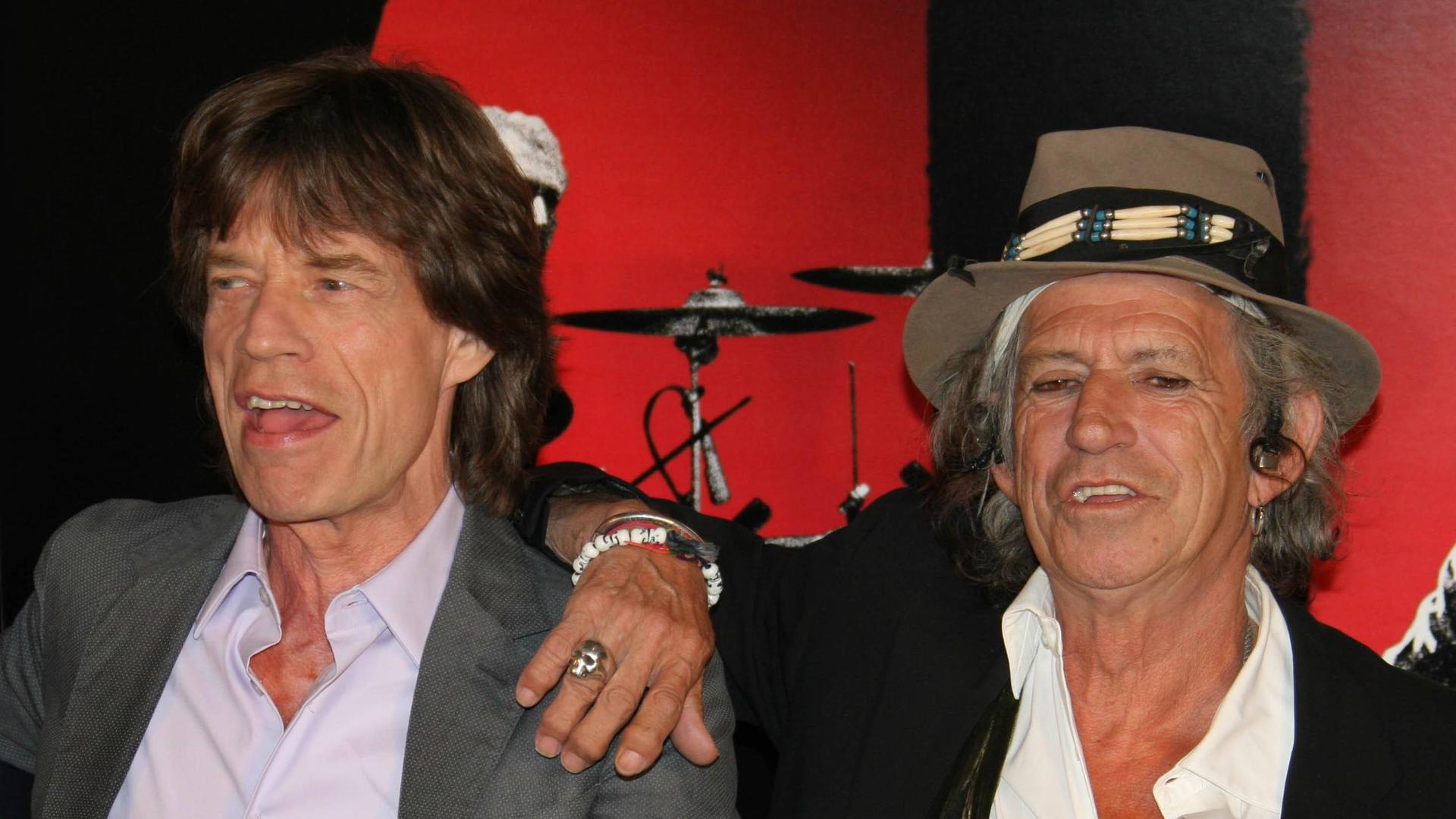 Die Musiker Mick Jagger und Keith Richards stehen gut gelaunt nebeneinander, im Hintergrund ein Schlagzeug Die Musiker Mick Jagger und Keith Richards stehen gut gelaunt nebeneinander, im Hintergrund ein Schlagzeug