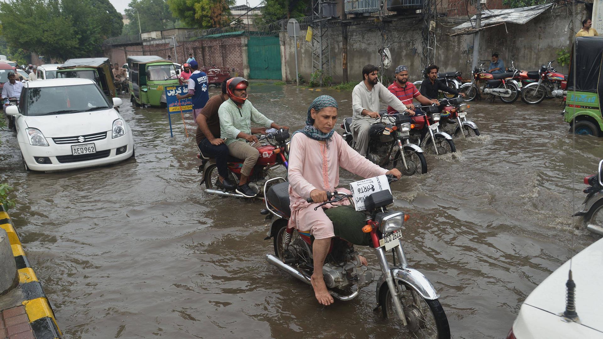 Nach heftigen Regenfällen sind die Straßen in Lahore, Pakistan, überflutet. Menschen kämpfen sich mit Mopeds durch die Straßen.