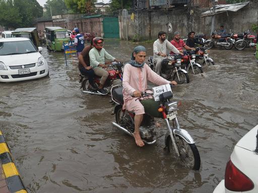 Nach heftigen Regenfällen sind die Straßen in Lahore, Pakistan, überflutet. Menschen kämpfen sich mit Mopeds durch die Straßen.