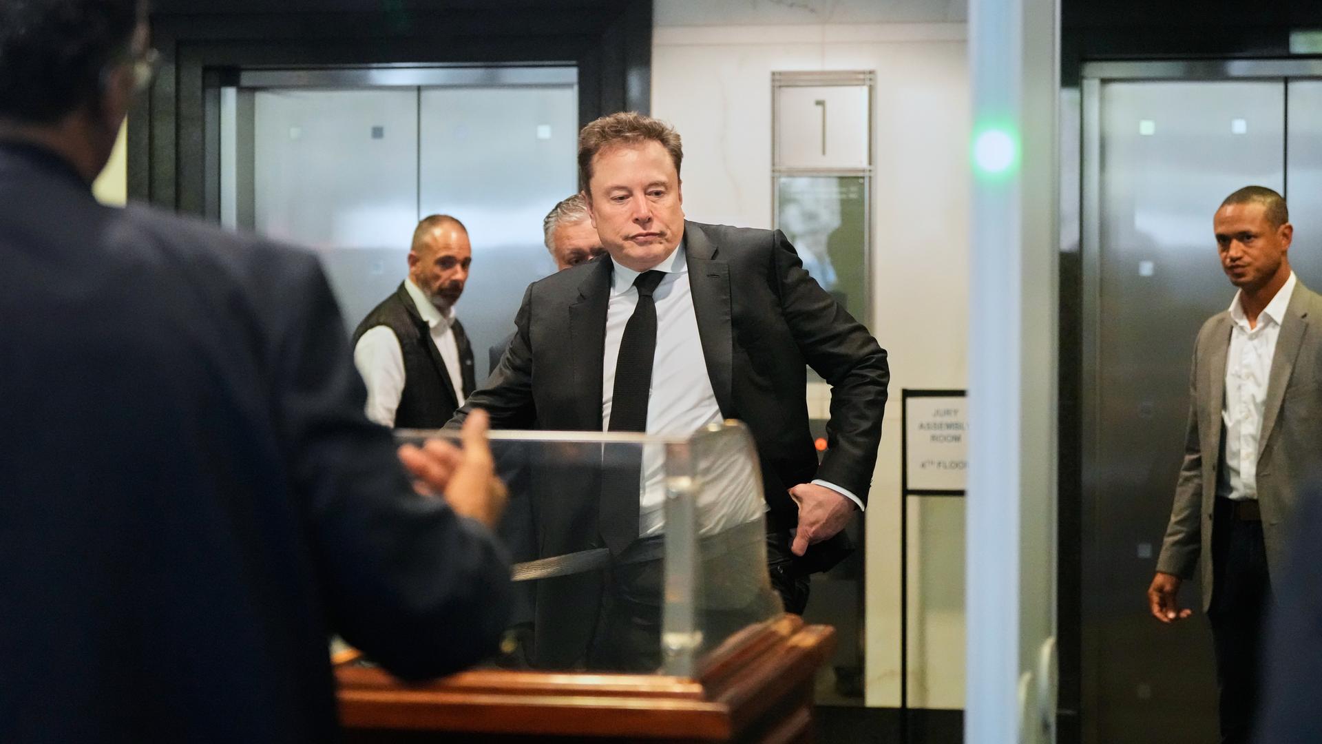 Elon Musk trifft am US-Bezirksgericht in Oakland, Kalifornien, ein. Um ihn herum stehen mehrere Personen. 
