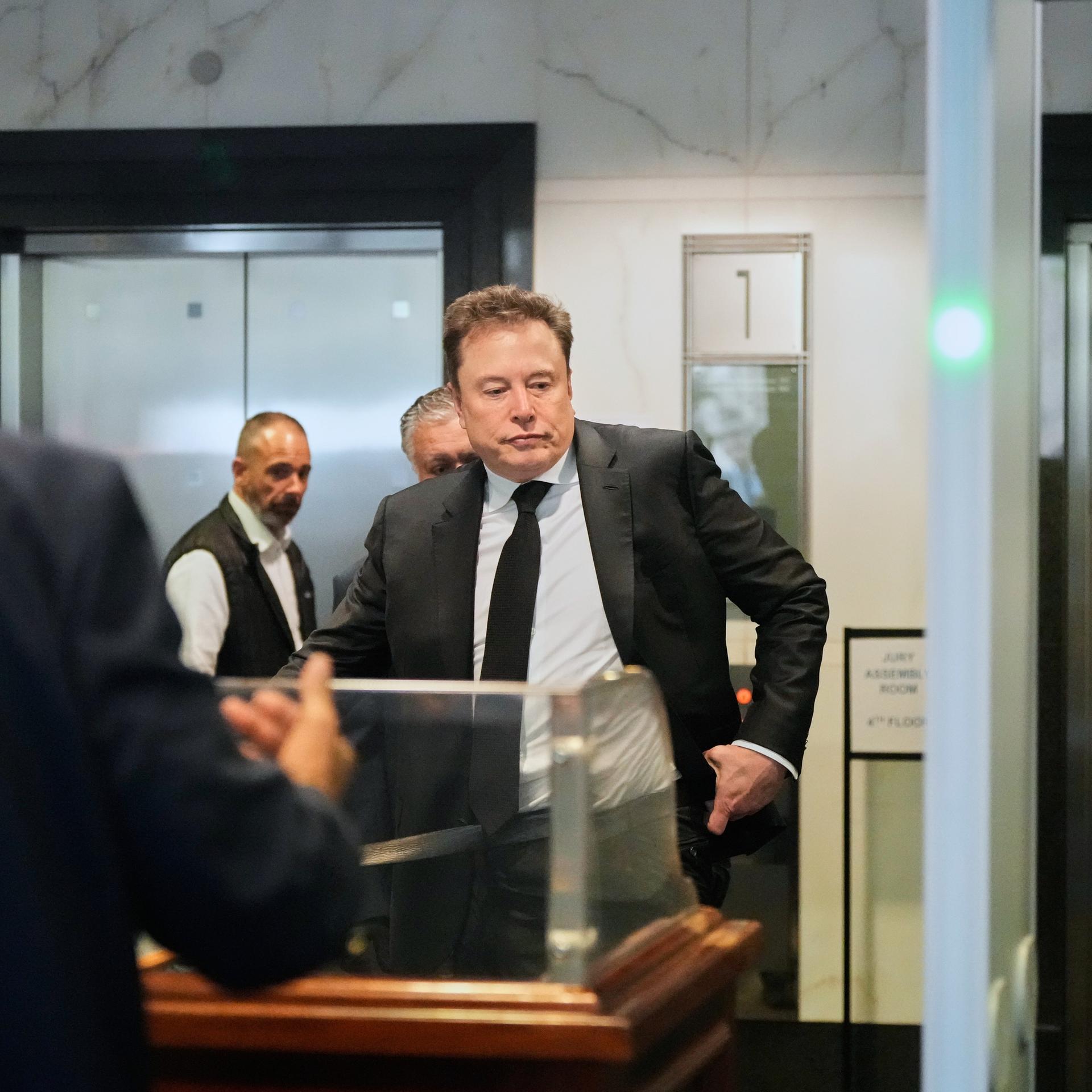 Elon Musk trifft am US-Bezirksgericht in Oakland, Kalifornien, ein. Um ihn herum stehen mehrere Personen. 