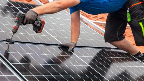 Ein Handwerker montiert eine Photovoltaikanlage auf dem Dach eines Einfamilienhauses.