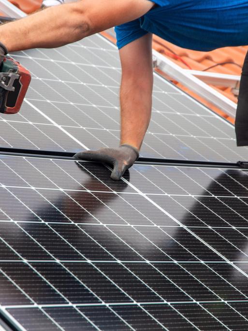 Ein Handwerker montiert eine Photovoltaikanlage auf dem Dach eines Einfamilienhauses.