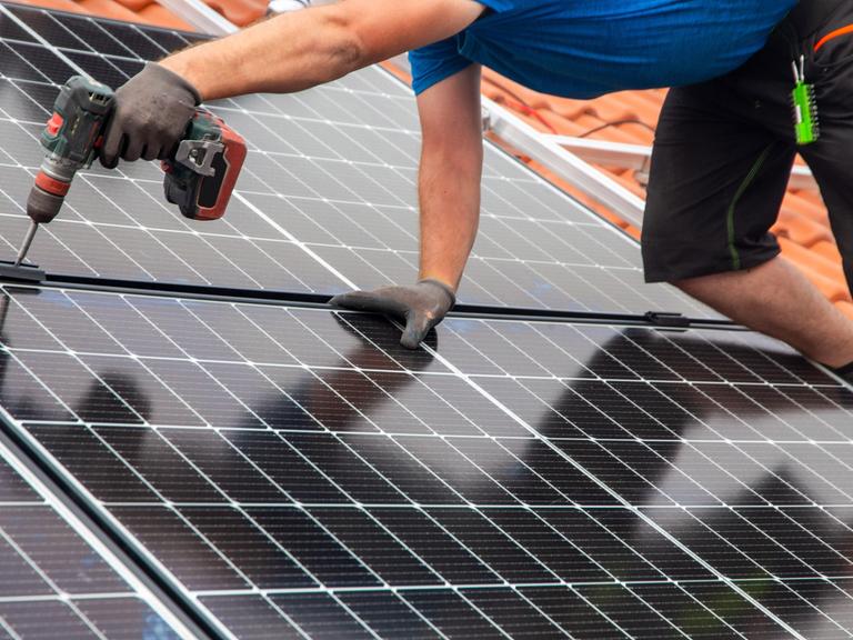 Ein Handwerker montiert eine Photovoltaikanlage auf dem Dach eines Einfamilienhauses.